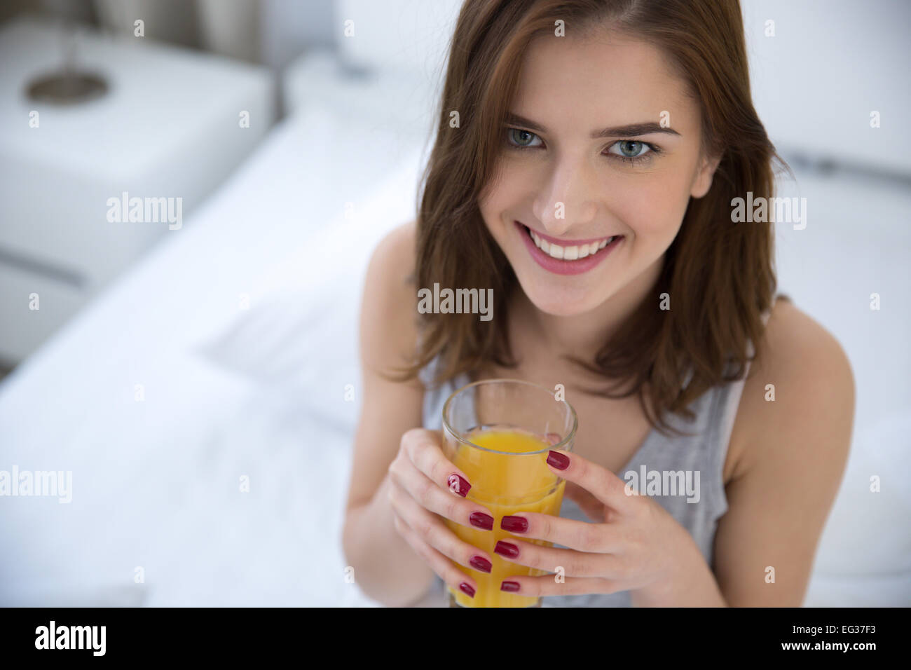 Glückliche Frau trinkt Orangensaft auf dem Bett Stockfoto