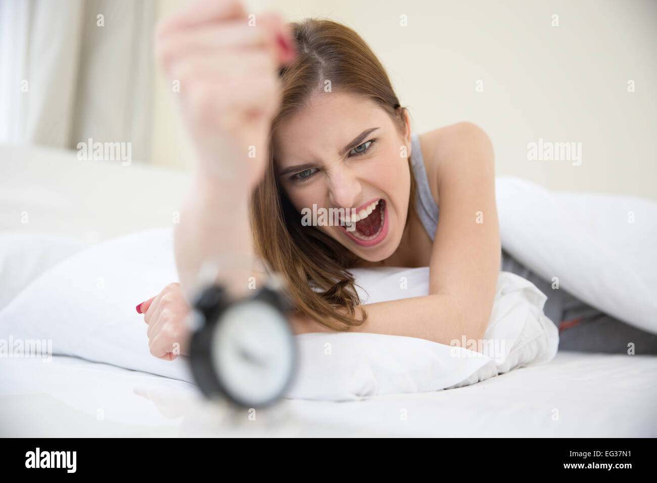 Böse Frau, die sehr früh aufgewacht, rufen Sie einen Wecker im Schlafzimmer Stockfoto