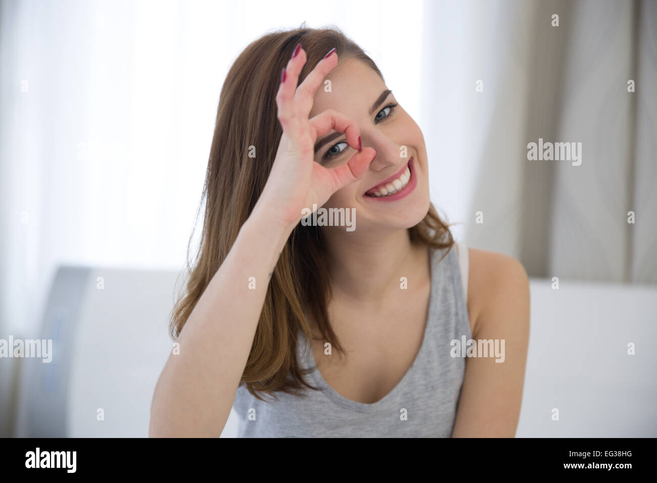 Glückliche Frau auf der Suche durch die Finger zu Hause Stockfoto