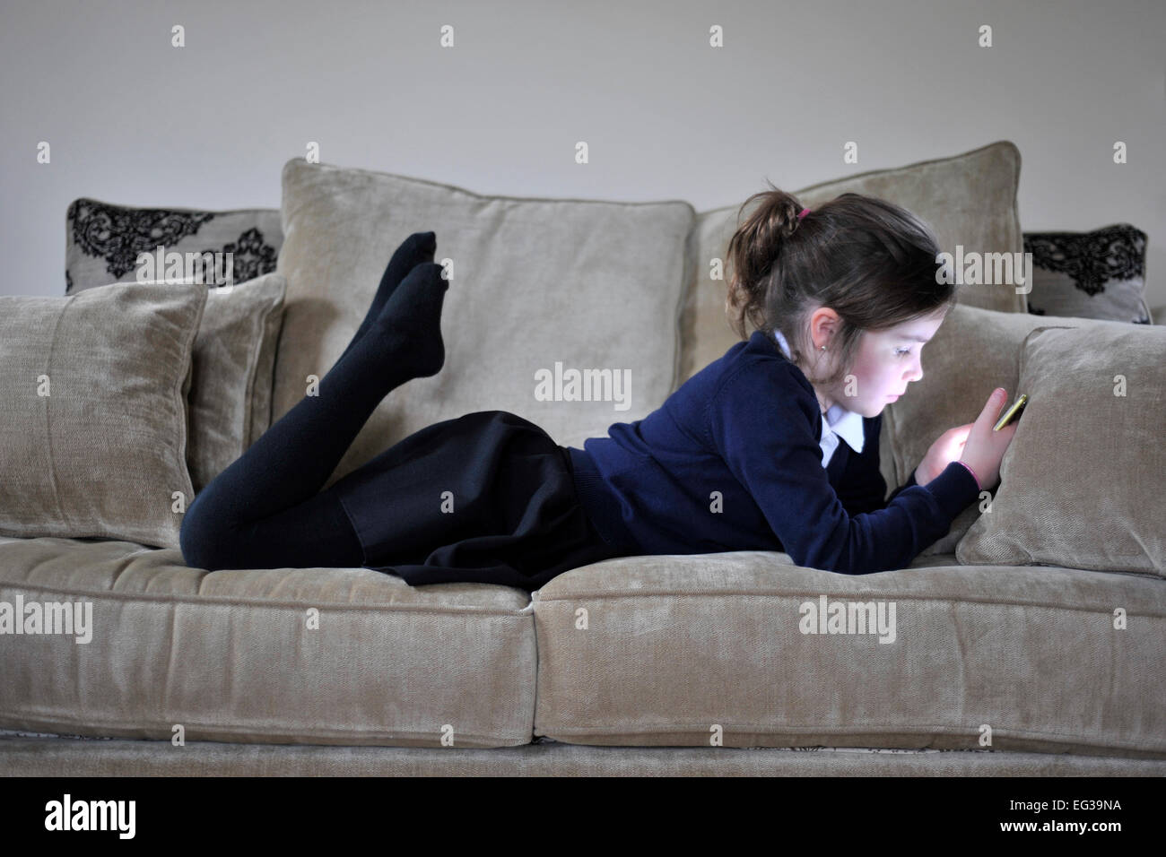 junges Mädchen in Schuluniform zu Hause mit handheld-Gerät Stockfoto