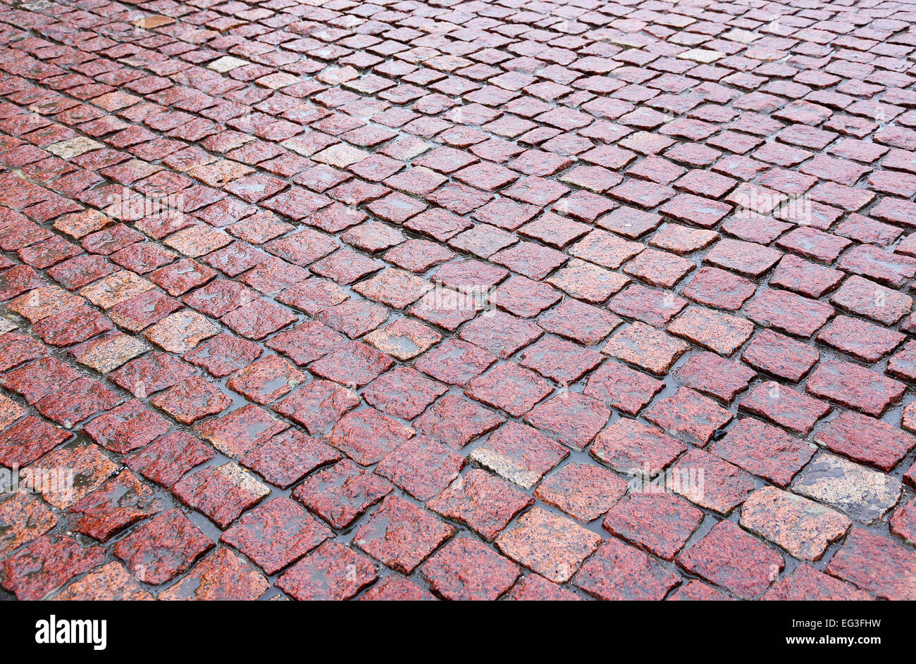 nasses Kopfsteinpflaster aus rotem Granit auf der Straße Stockfoto