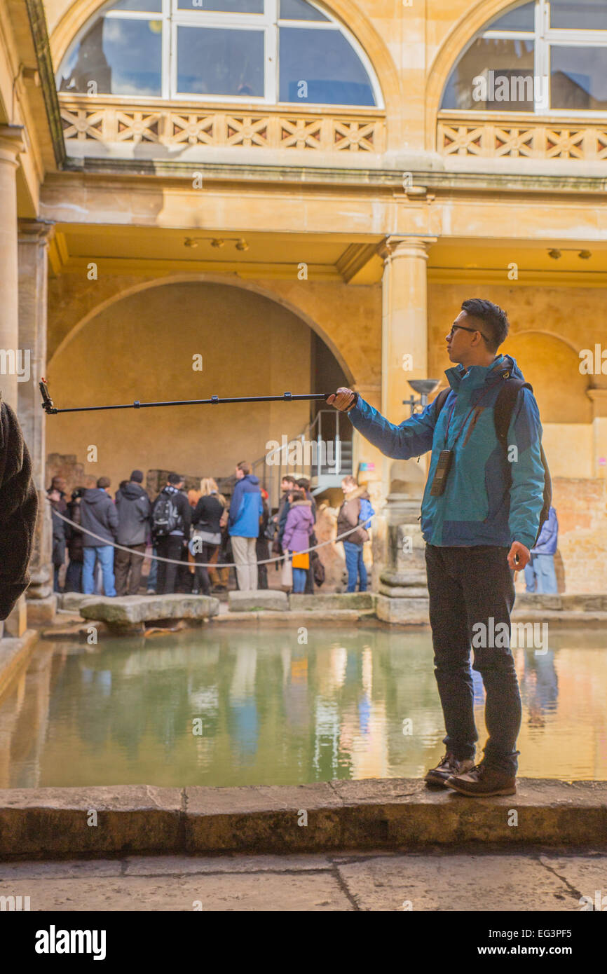Ein Tourist nimmt ein Bild von sich selbst mit einem Selfie-Stick an der Seite von Roman Baths in Bath, Großbritannien stehen. Stockfoto