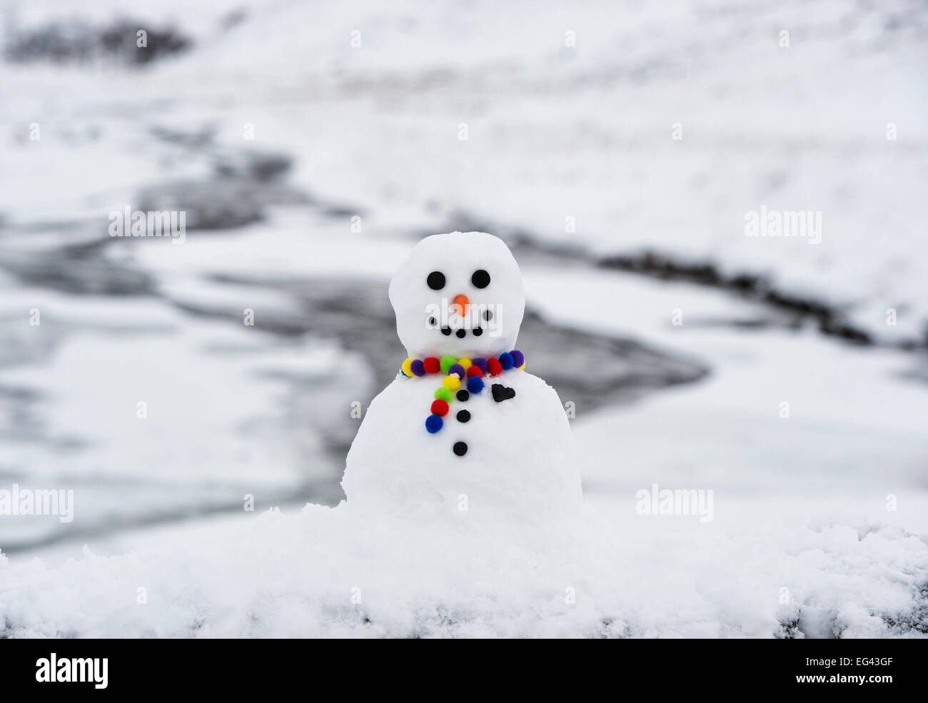 Glücklich Schneemann mit einem großen Kohle Herz auf einer Wand in der winterlichen schottischen Landschaft Stockfoto