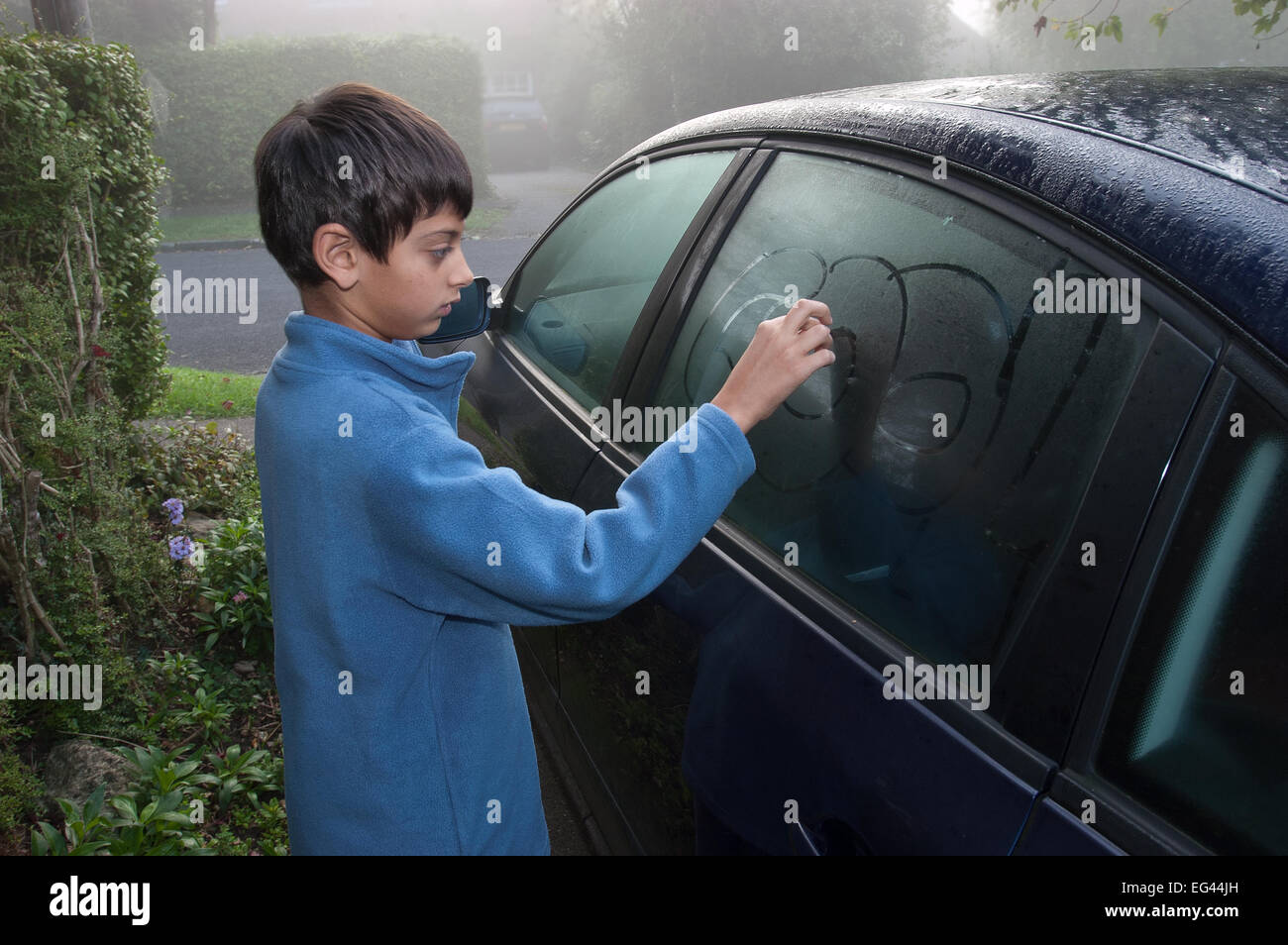 Junge Grundschule junge Zeichnung im und am Autofenster auf feuchten nebligen Morgen vor der Schule laufen Stockfoto