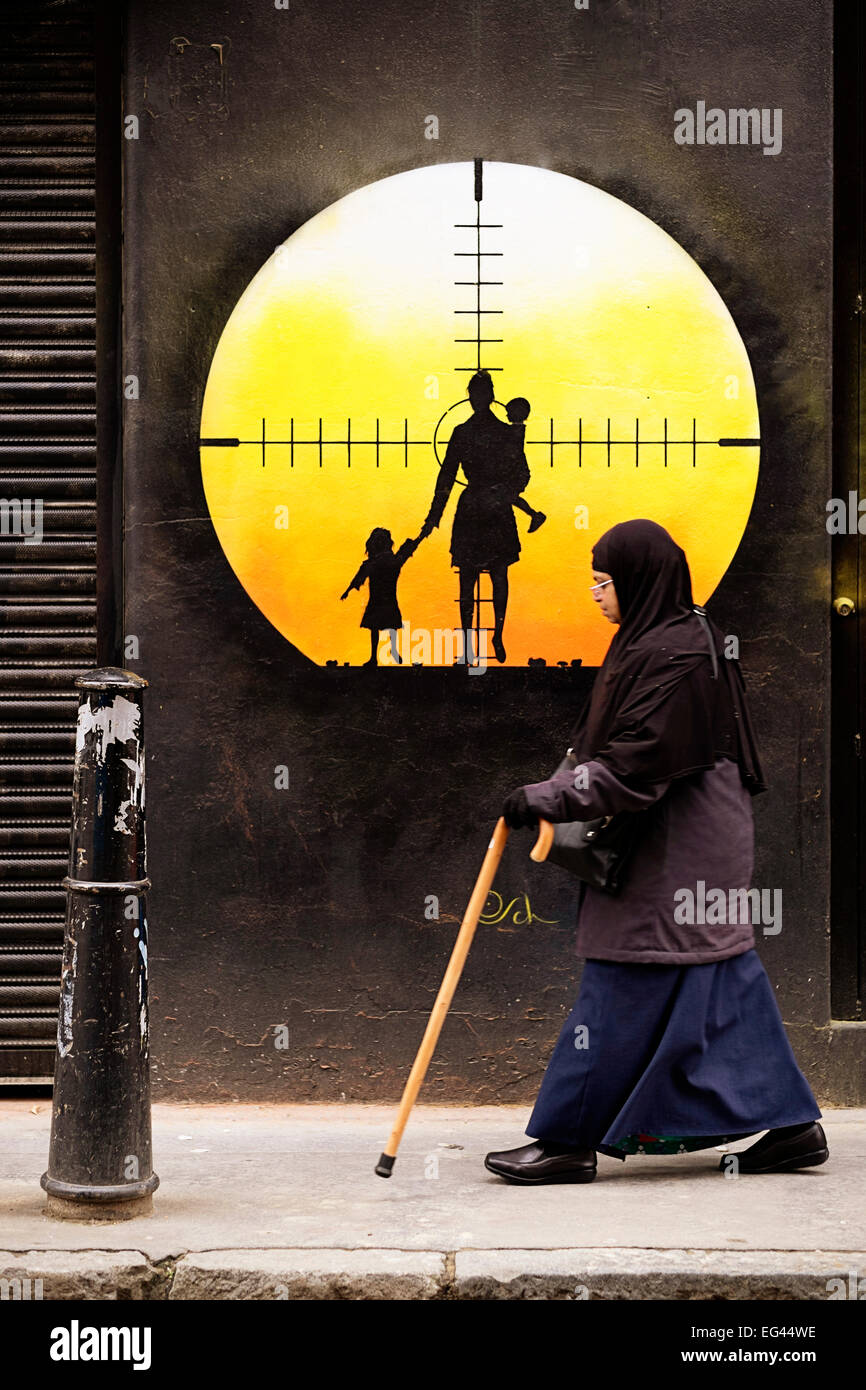 Ältere muslimische Frau geht vorbei an einem gemalten Ziel mit einer Frau mit Kindern in einem Scharfschützen Sehvermögen in East London, UK Stockfoto