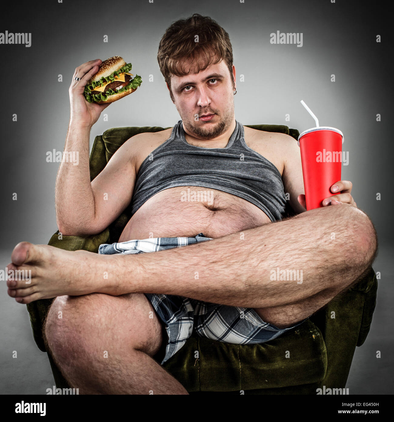 Dicker Mann Essen Hamburger auf Sessel sitzend. Stil-Fast-Food. Stockfoto