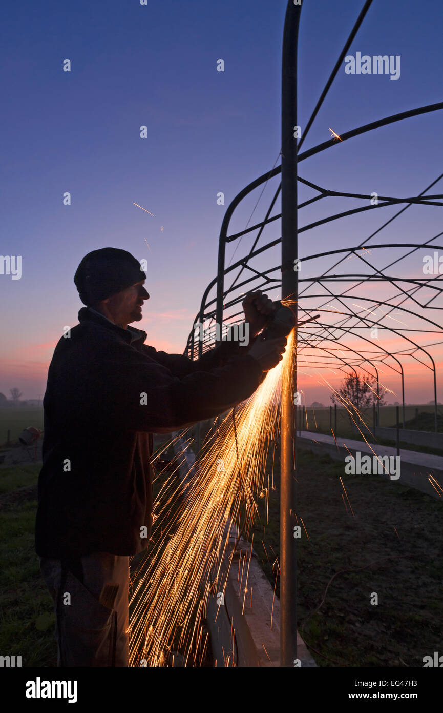 Junger Mann Schleifen auf einem Metallrahmen in der Abenddämmerung, Funken fliegen, Othenstorf, Mecklenburg-Western Pomerania, Deutschland Stockfoto