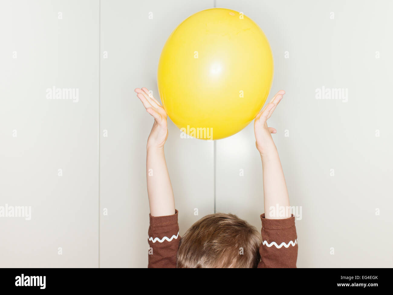 Kind hält gelben Ballon mit erhobenen Armen über den Kopf. Lustige Kindheit Moment. Stockfoto