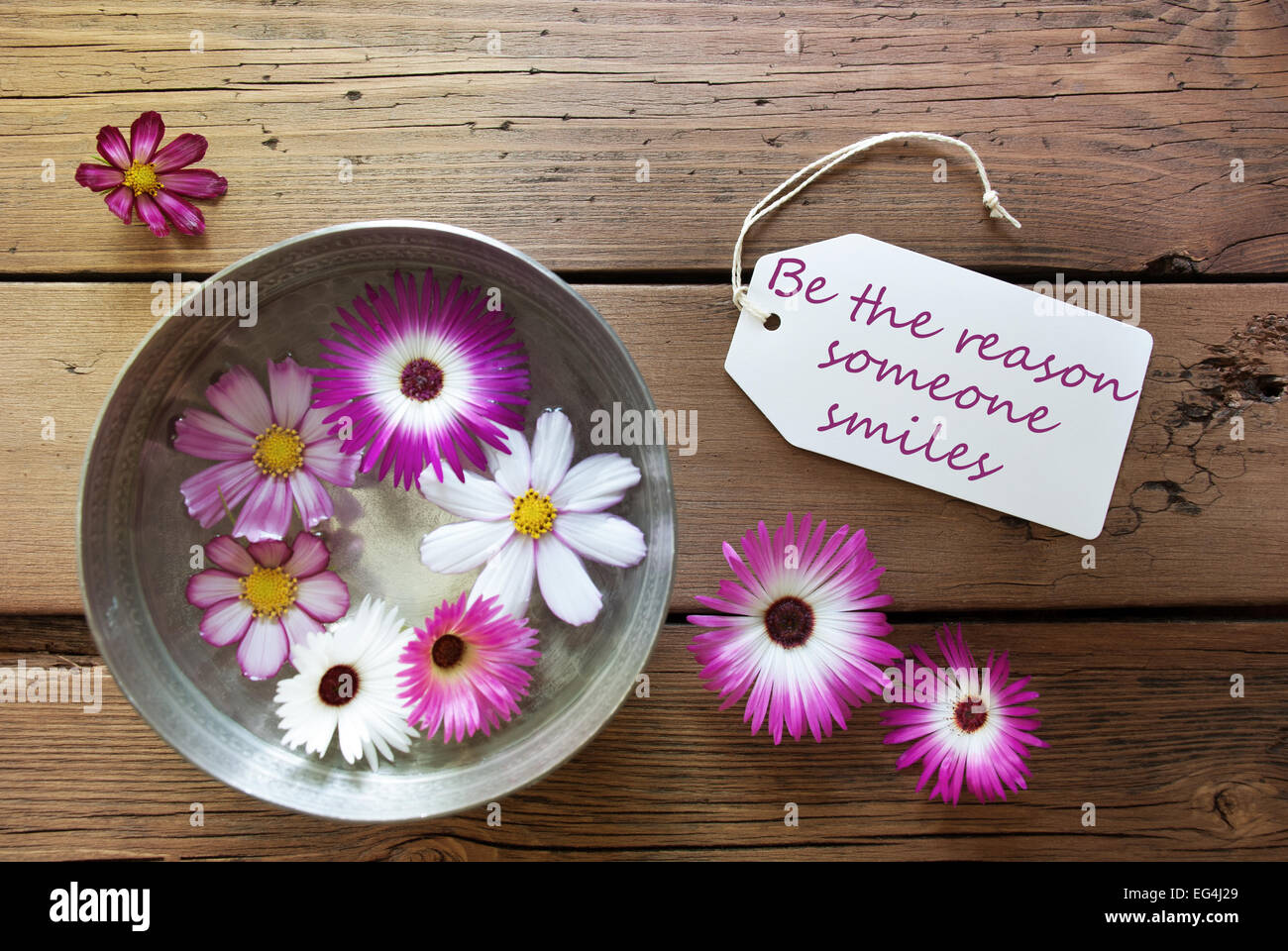 Silberschale mit Etikett mit Leben-Zitat werden der Grund, warum, den jemand lächelt, mit einer lila und weißen Blüten auf hölzernen Hintergrund V Stockfoto