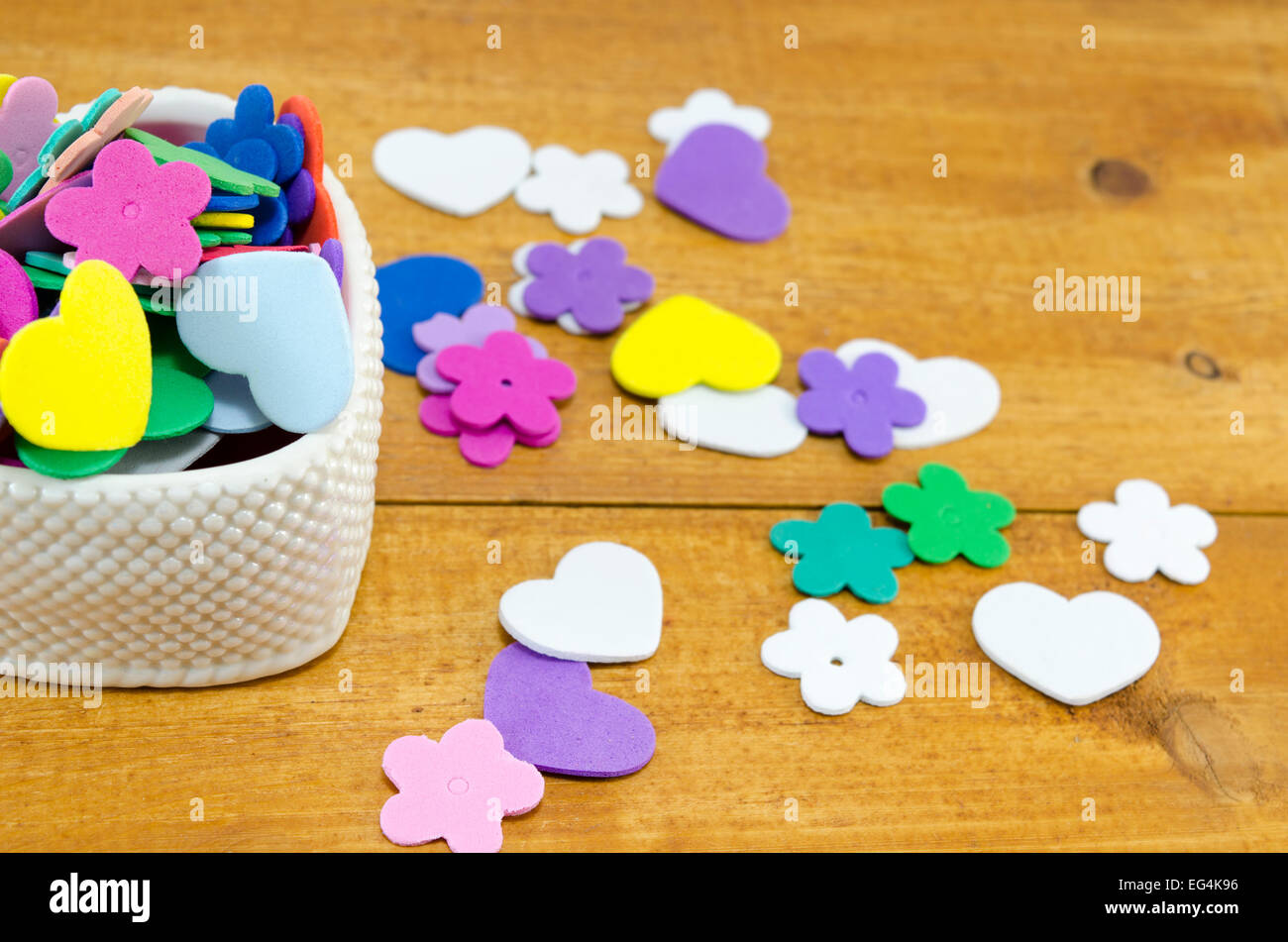 Herzförmige Box gefüllt mit bunten Papier-Herzen und Blumen auf einem hölzernen Hintergrund Stockfoto