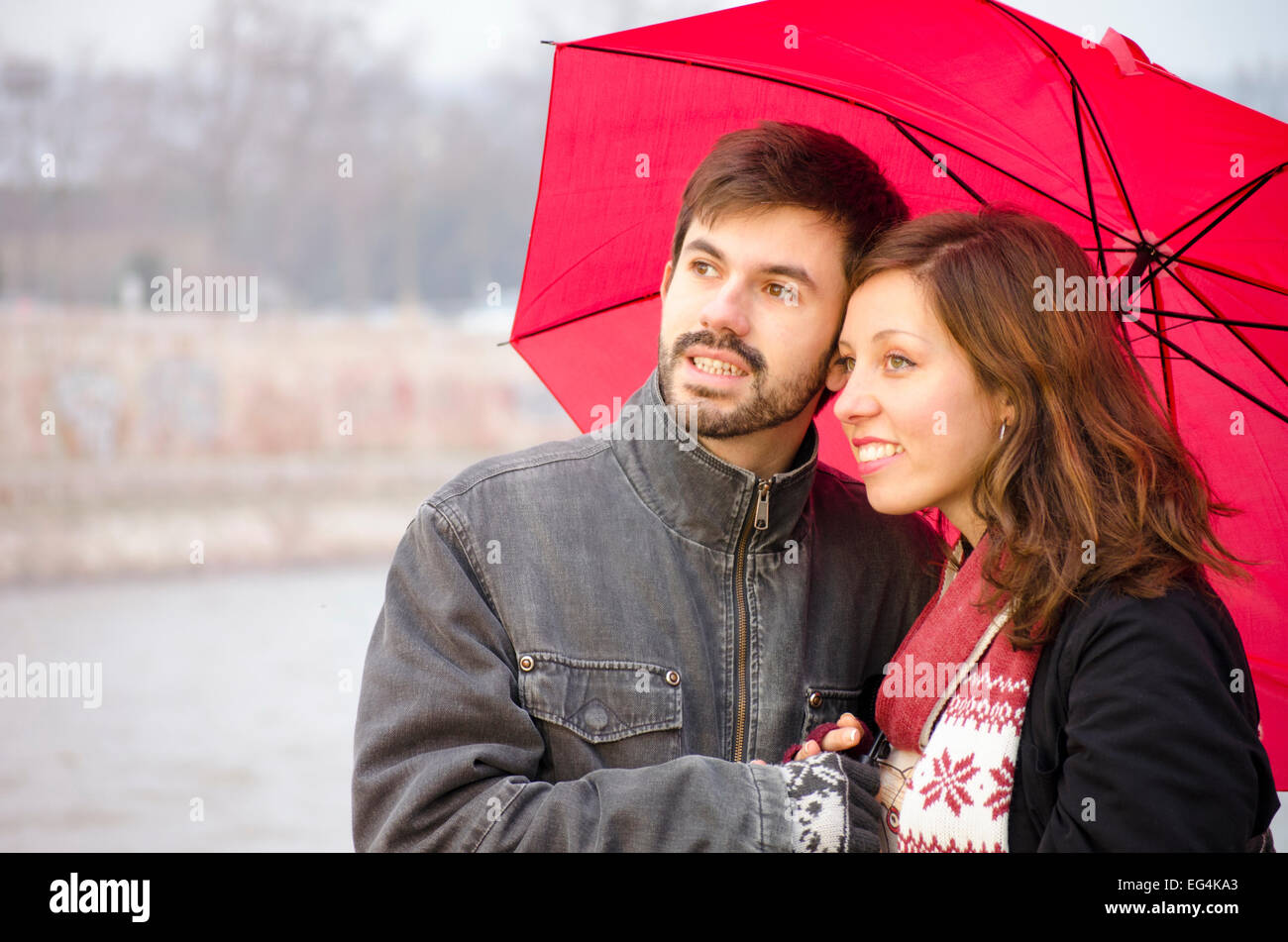Frau und ein bärtiger Mann in einem roten Regenschirm an einem regnerischen Tag im Freien, Stockfoto