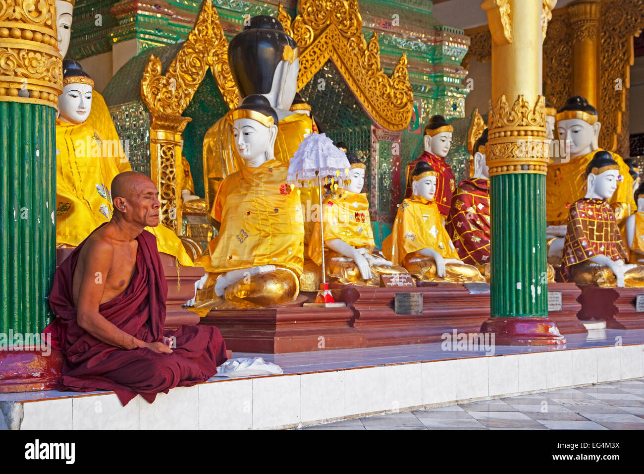 Buddhistischer Mönch betend vor Buddha-Statuen in der Shwedagon Zedi Daw-Pagode in Yangon / Rangun, Myanmar / Burma Stockfoto