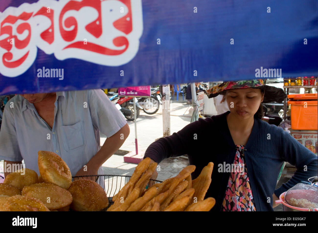 Ein Mann & Frau sind verschiedene Brot in heißem Öl kochen und servieren es als Straße Nahrung auf eine Stadt Straße in Phnom Penh, Kambodscha. Stockfoto