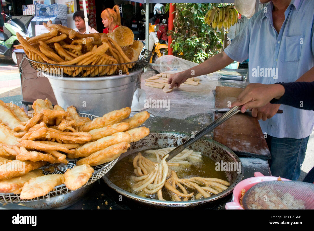 Ein Mann & Frau sind verschiedene Brot in heißem Öl kochen und servieren es als Straße Nahrung auf eine Stadt Straße in Phnom Penh, Kambodscha. Stockfoto