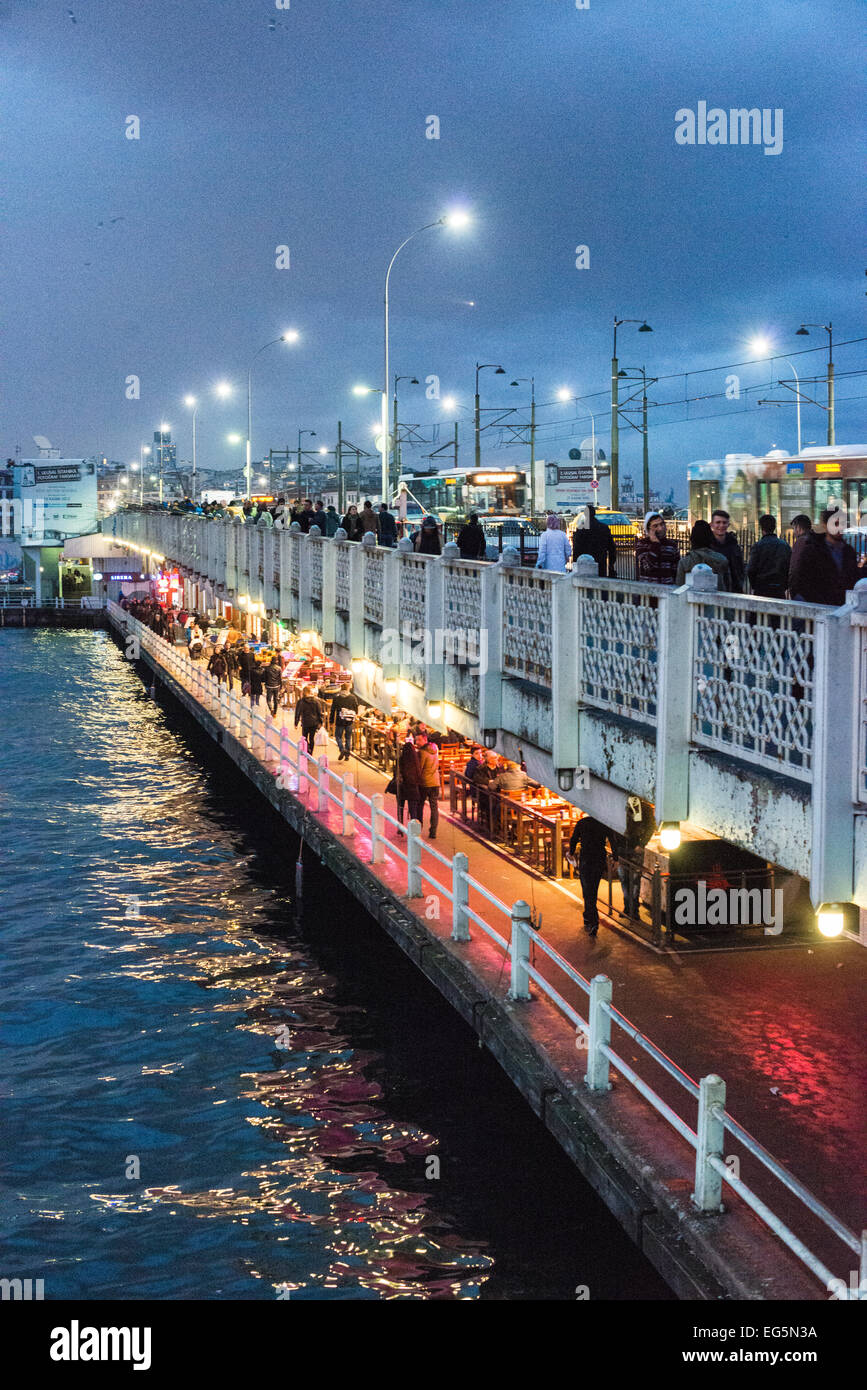 Galata Bridge Restaurants Goldenes Horn Istanbul Türkei // ISTANBUL, Türkei — die Galata Bridge mit zwei Ebenen überspannt das Goldene Horn in der Abenddämmerung, deren charakteristisches zweistufiges Design im Abendlicht beleuchtet wird. Auf dem oberen Deck der Brücke befinden sich Fahrzeuge und Fußgänger, während im unteren Stockwerk Restaurants und Cafés untergebracht sind. Das 490 Meter hohe Gebäude dient sowohl als wichtige Verkehrsanbindung als auch als beliebtes abendliches Ziel. Stockfoto