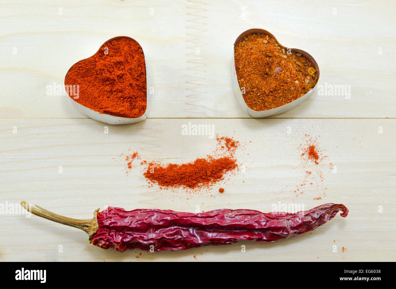 Getrocknete Paprika und Pfeffer in Herzform Container auf einem Holztisch, bilden ein Smiley-Gesicht Stockfoto