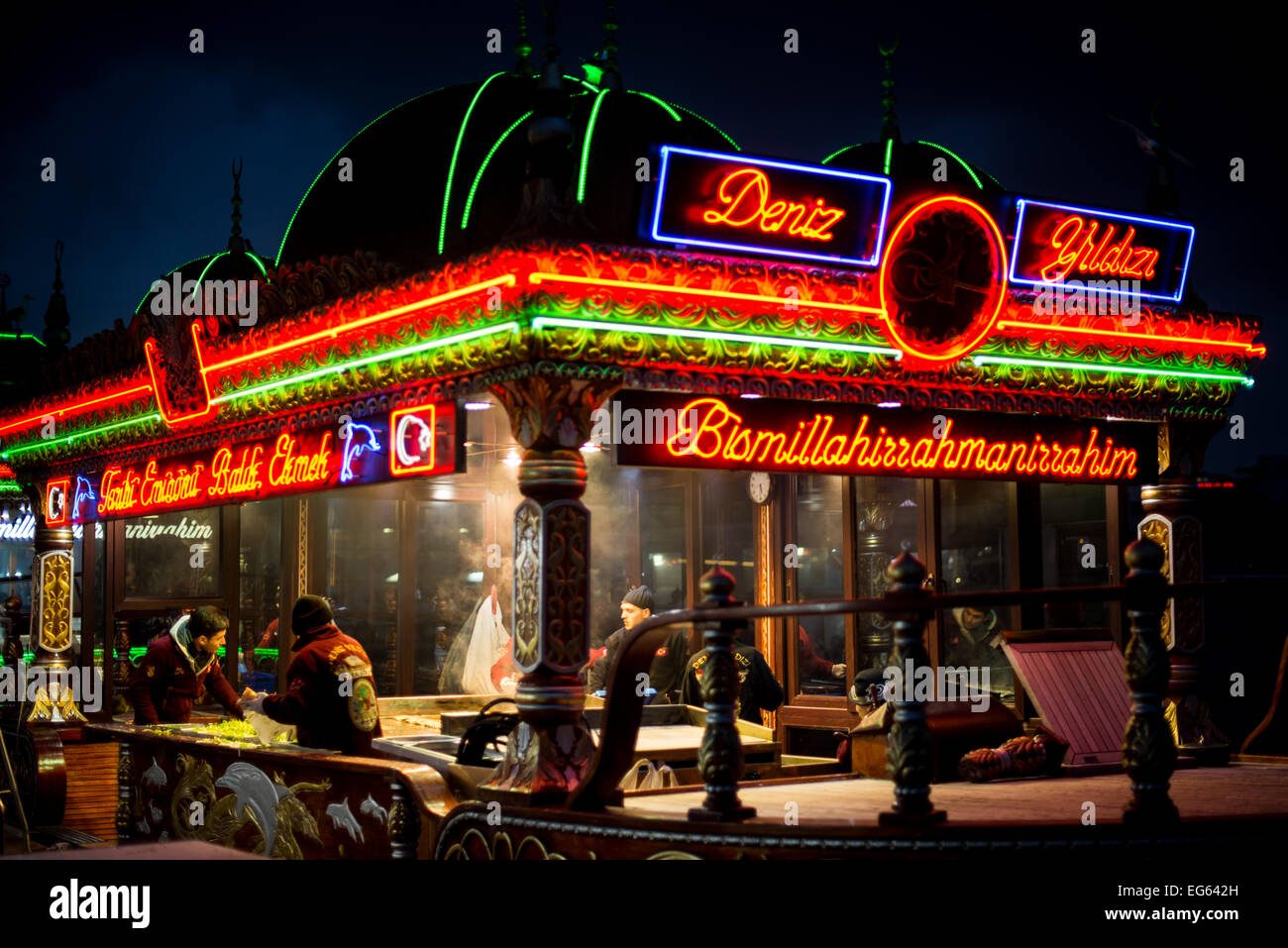 Balik Ekmek schwimmende Restaurants Eminonu Istanbul Türkei // ISTANBUL, Türkei - beleuchtete balik Ekmek Boote servieren traditionelle Fischsandwiches an der Eminonu Uferpromenade in der Nähe der Galata Brücke. Diese schwimmenden Restaurants, die in der Region als balıkçı tekneleri bekannt sind, bieten gegrillte Makrele in Weißbrot mit Zwiebeln und Salat als beliebtes Street Food an. Die kunstvoll verzierten Boote sind im osmanischen Stil gehalten und bleiben dauerhaft an der historischen Wasserfront des Goldenen Horns verankert. Eminonu dient als wichtiger Fährhafen und Geschäftsviertel, der die europäische und asiatische Seite verbindet Stockfoto