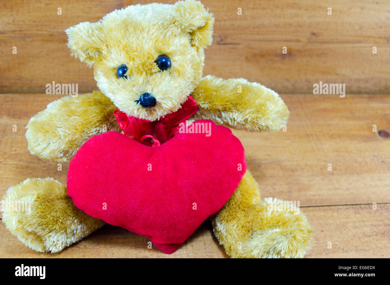 Brauner Teddybär umarmt ein großes rotes Herz auf einem Holztisch Stockfoto