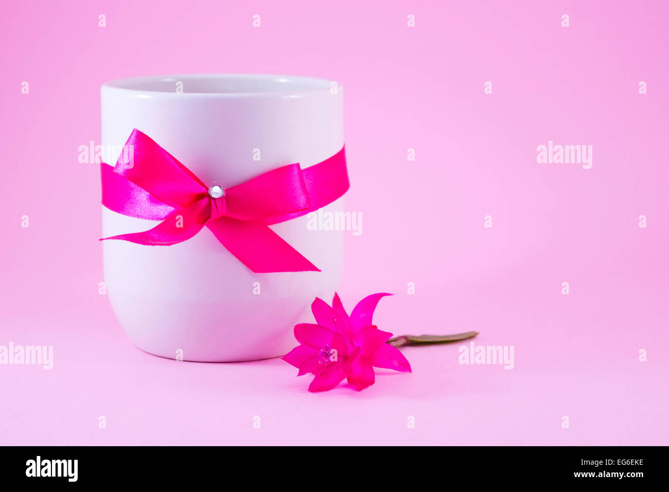 Weiße Kaffeetasse verziert mit einer rosa Schleife und eine rosa Blume Stockfoto