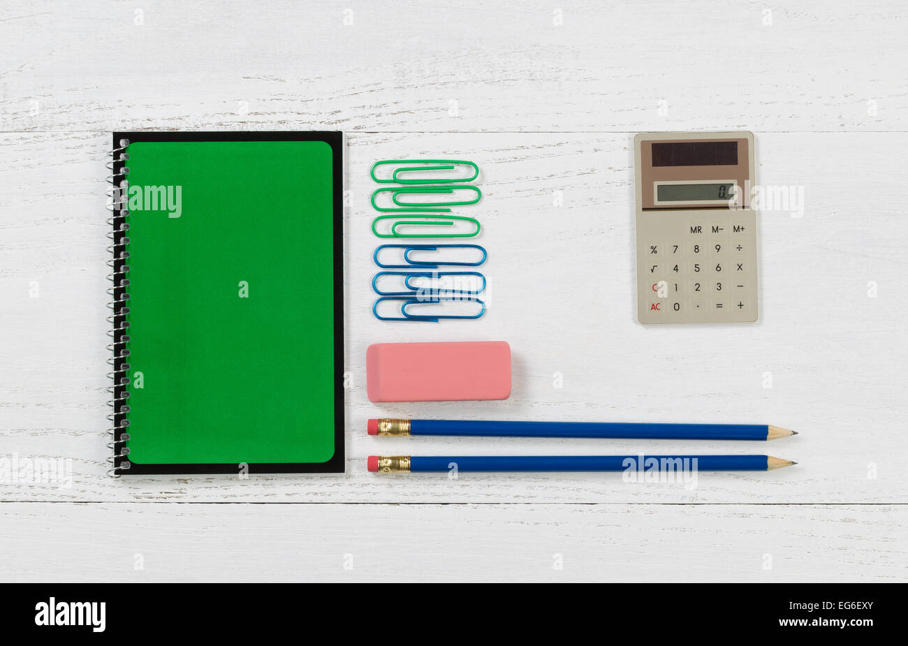 Grüne Spirale Notizblock mit Bleistift, Radiergummi, Taschenrechner und Büroklammern auf Desktop. Stockfoto