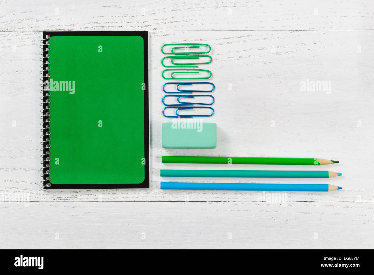 Grüne Spirale Notizblock mit Bleistift, Radiergummi und Büroklammern auf Desktop. Muster in den Farben Grün und blau mit einem weißen Holz b Stockfoto