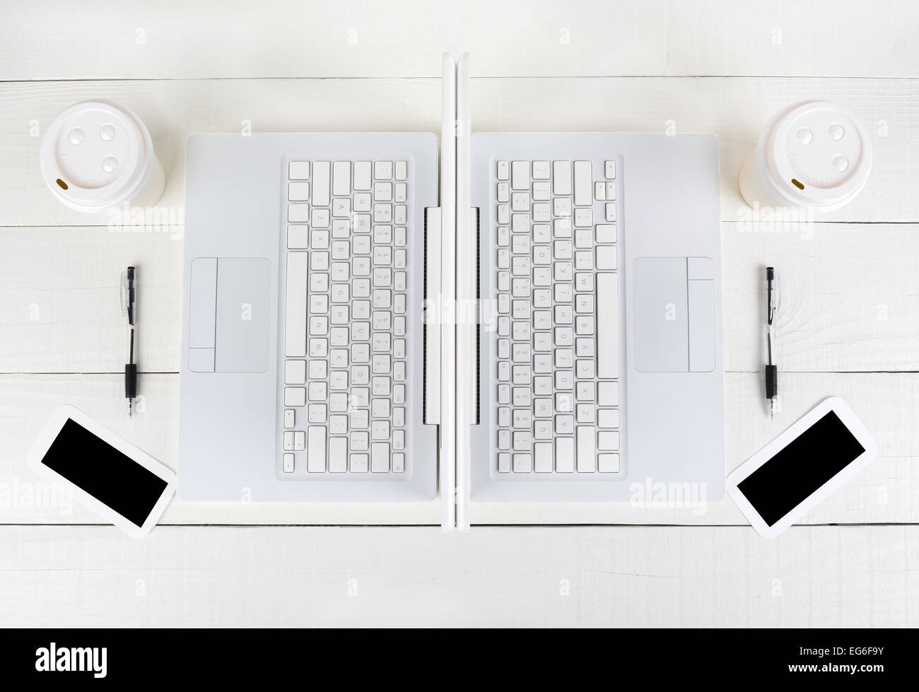 Hohen Winkel Schuss zwei Laptop-Arbeitsplätze mit fast identische Layouts Rücken an Rücken. Querformat auf einem weißen Holztisch. Stockfoto