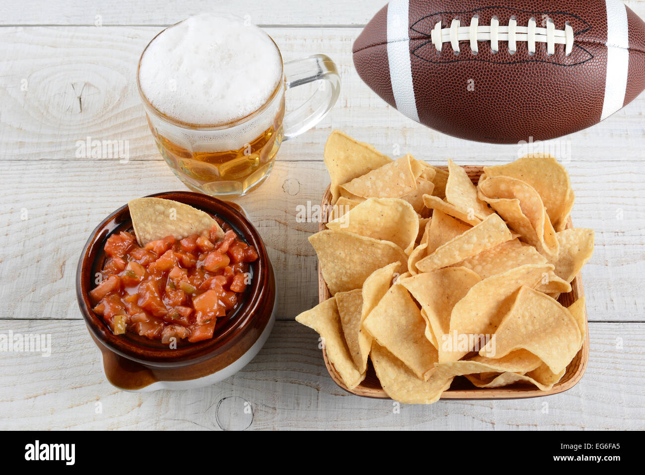 Hohen Winkel geschossen einer Schüssel Mais-Chips ein Topf voller Frische Salsa einen Becher Bier und ein American Football auf einem weiß getünchten Rost Stockfoto