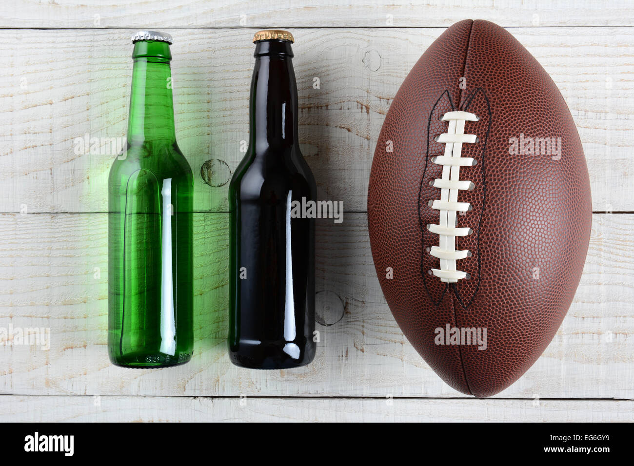 Zwei Bierflaschen und ein amerikanisches Fußball auf einem rustikalen weiß getünchten Holzoberfläche. Querformat. Eine grüne Flasche und Stockfoto