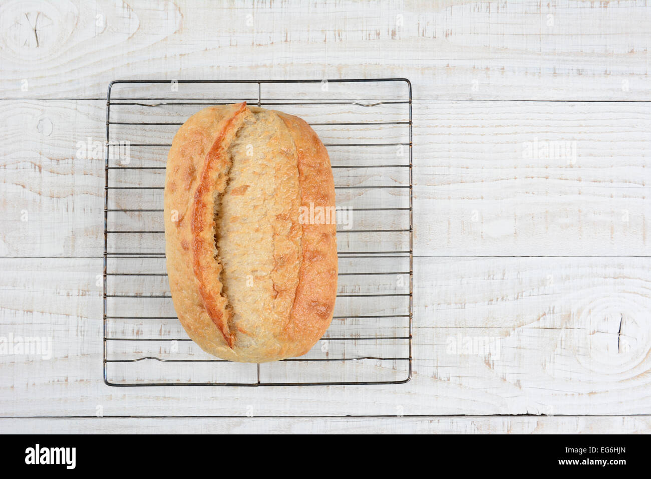 Hohen Winkel Schuss einen frisch gebackenen Laib Brot auf ein Kuchengitter. Querformat auf einem rustikalen weiß getünchten Küchentisch mit Stockfoto