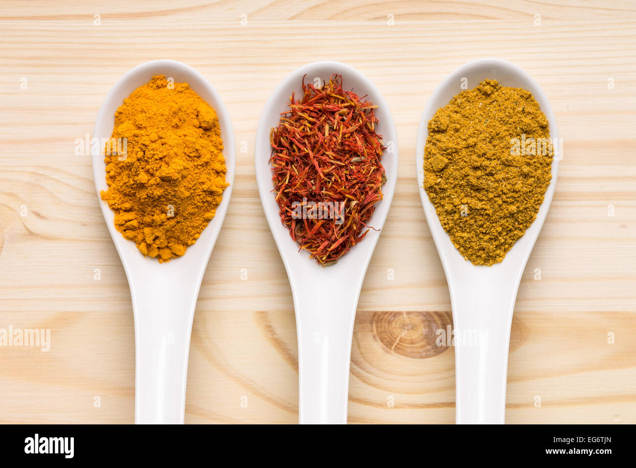 Verschiedenen Gewürzen auf hölzernen Hintergrund. Zafaran, Khmeli-Suneli und Kurkuma in Keramik Löffel Stockfoto