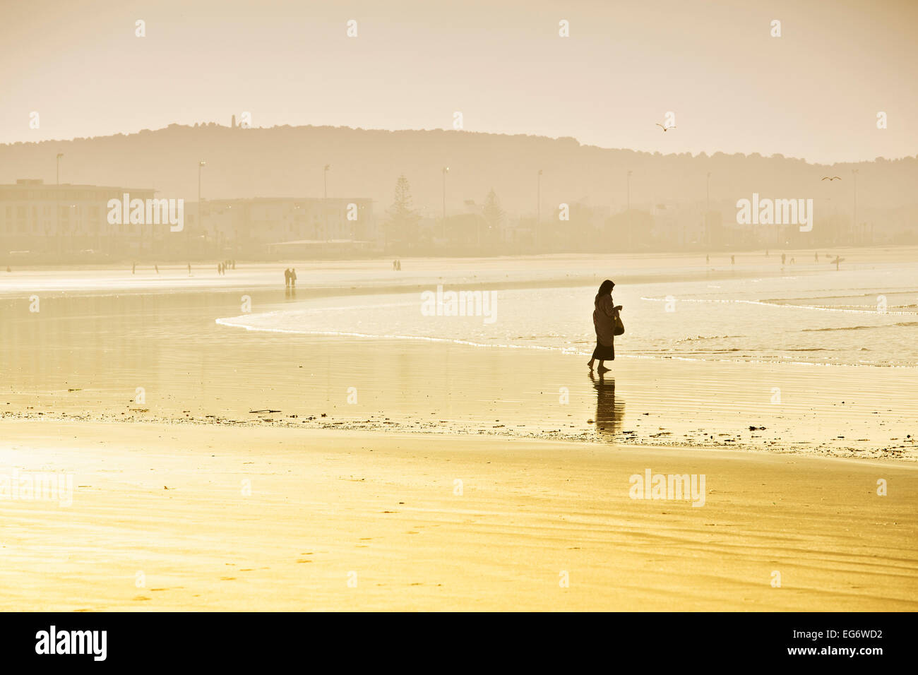 Rambler mit Kopftuch auf dem Strand, Silhouette im Morgenlicht, Plage Tagharte, Essaouira, Marokko Stockfoto