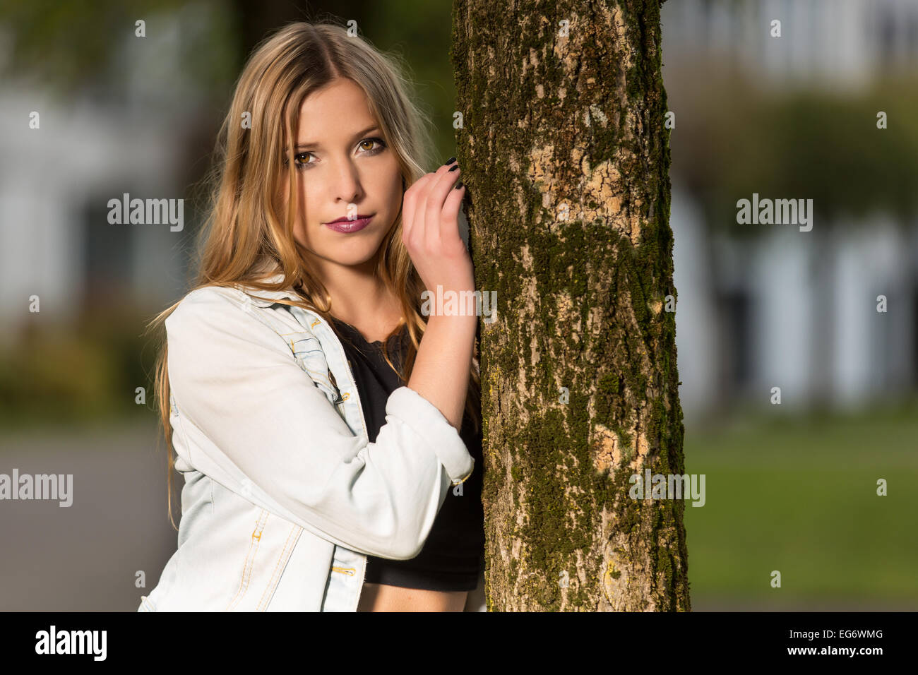 Junge Frau, die an einen Baumstamm gelehnt Stockfoto