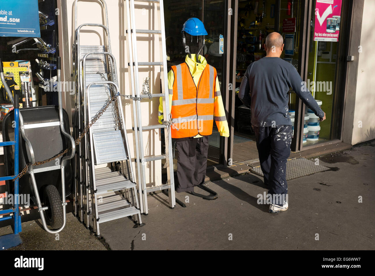 Mann, der eine ähnliche Größe geht vorbei an Sicherheitskleidung Show vor einem Hardwear-Geschäft. Wie zwei Figuren von echten und falschen Arten. London, UK. Stockfoto