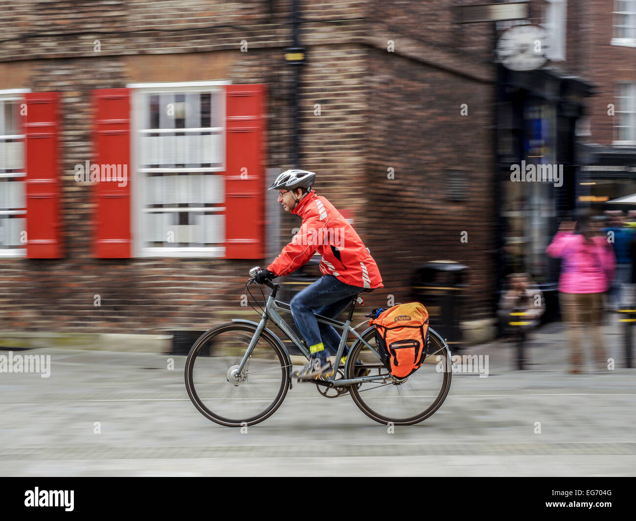 Mann in Orange Jacke einen Pendler Pendler fahren graue grauen Fahrrad Zyklus Fahrrad mit Motion blur der Hintergrund. Stockfoto