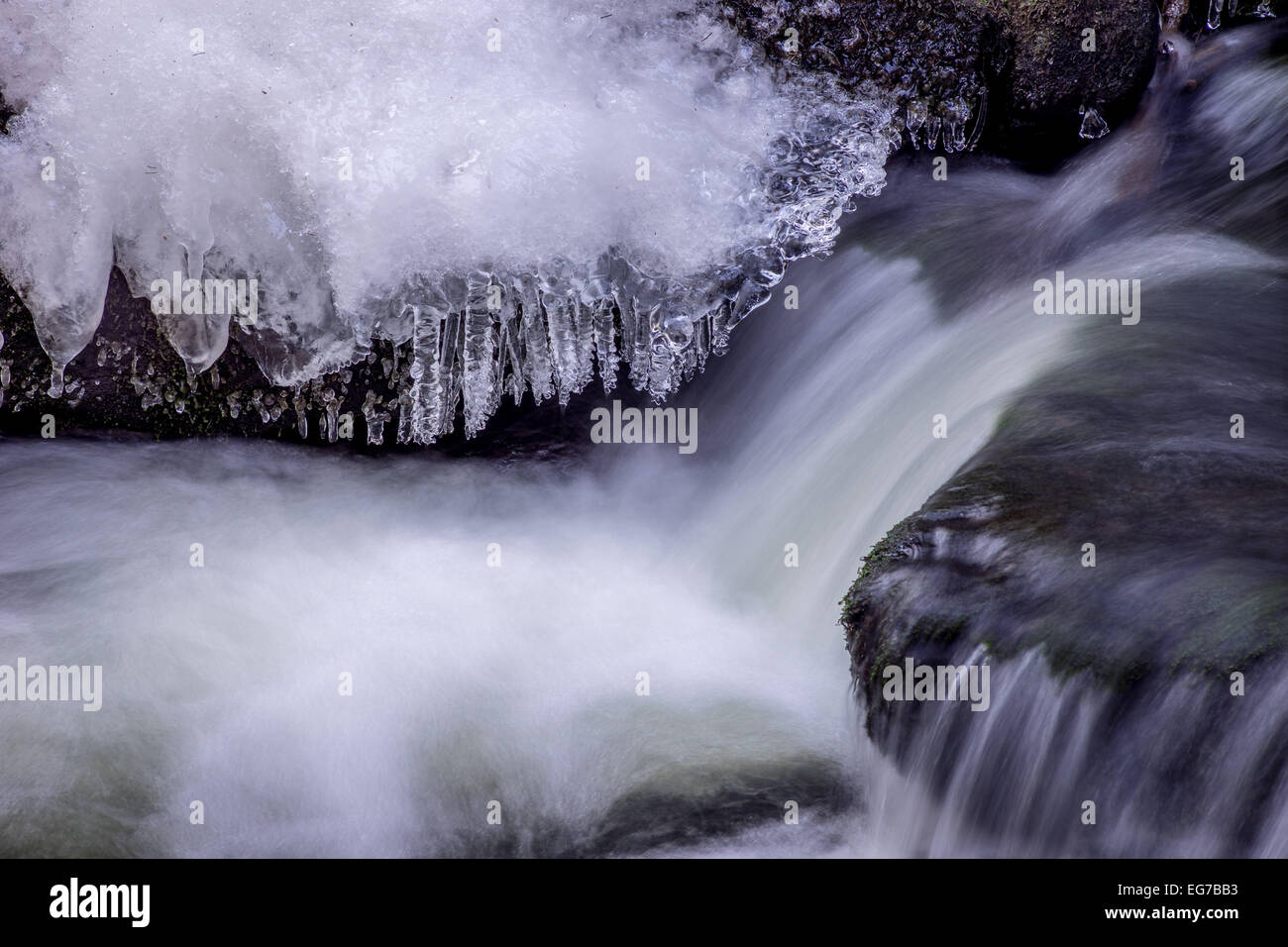 Eiszapfen auf Felsbrocken und fließendes Wasser Stockfoto