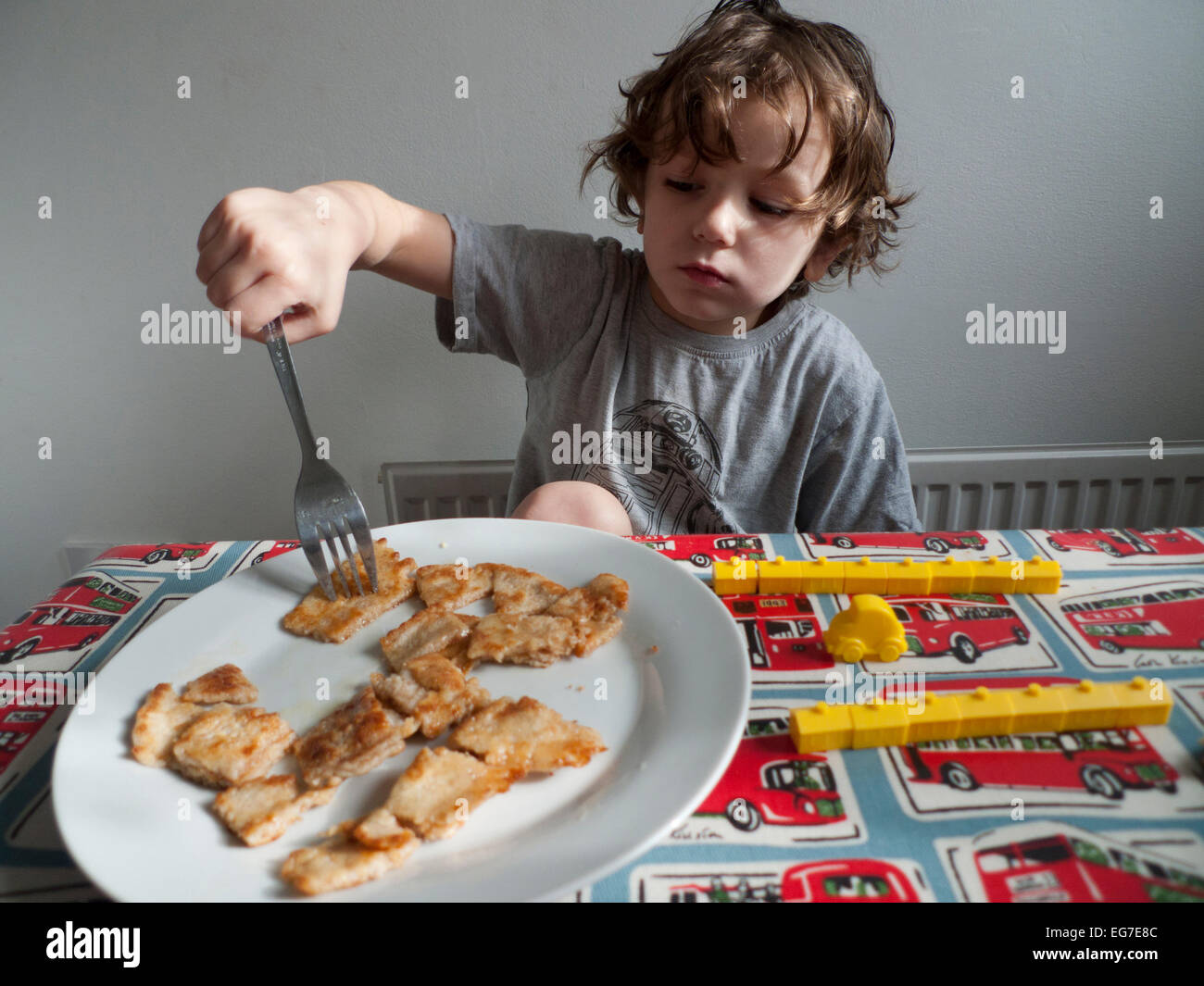 Ein 5 Jahre alter Junge am Frühstückstisch auf Pfannkuchen Tag sitzen essen Pfannkuchen spielen mit kleinen gelben Monopol Häuser UK KATHY DEWITT Stockfoto
