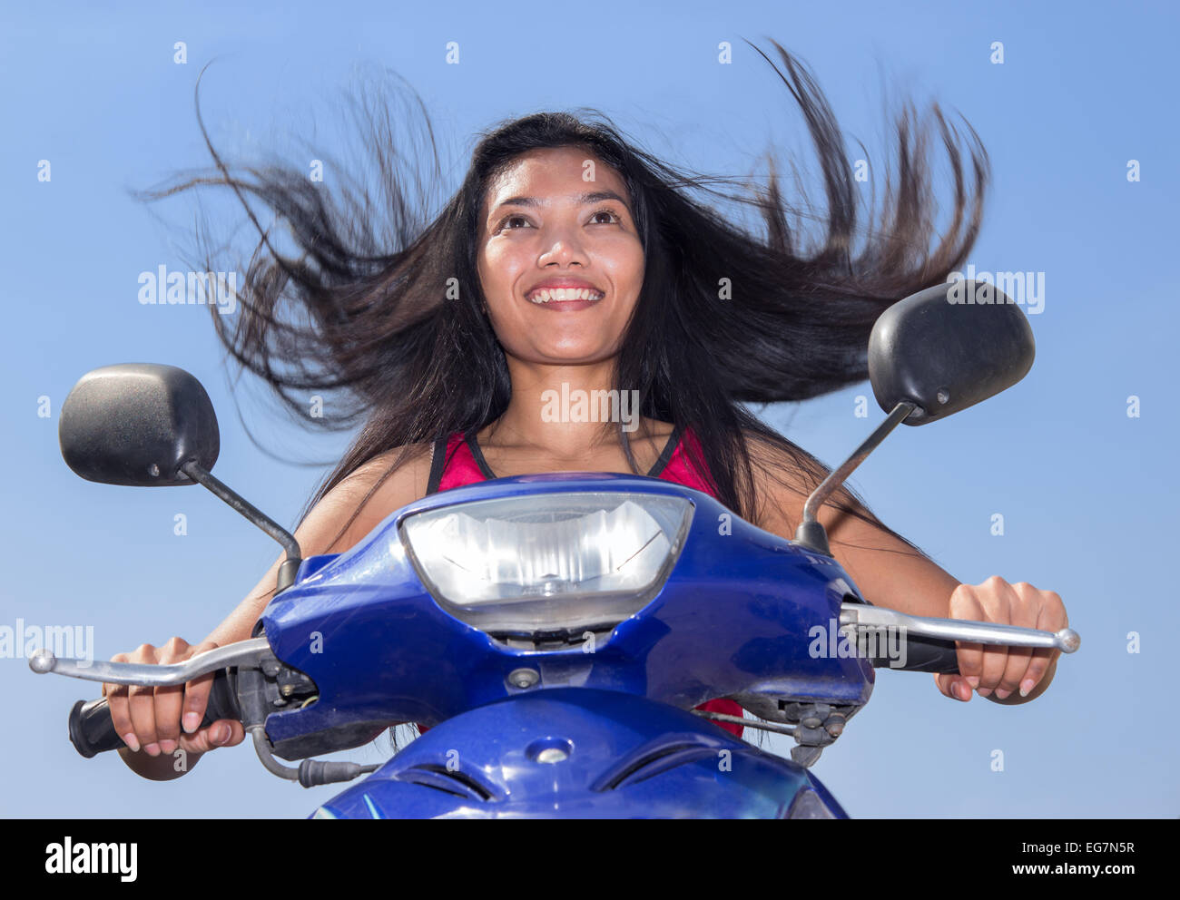 Frau mit fliegenden Haare auf einem Motorrad auf einem blauen Hintergrund Stockfoto