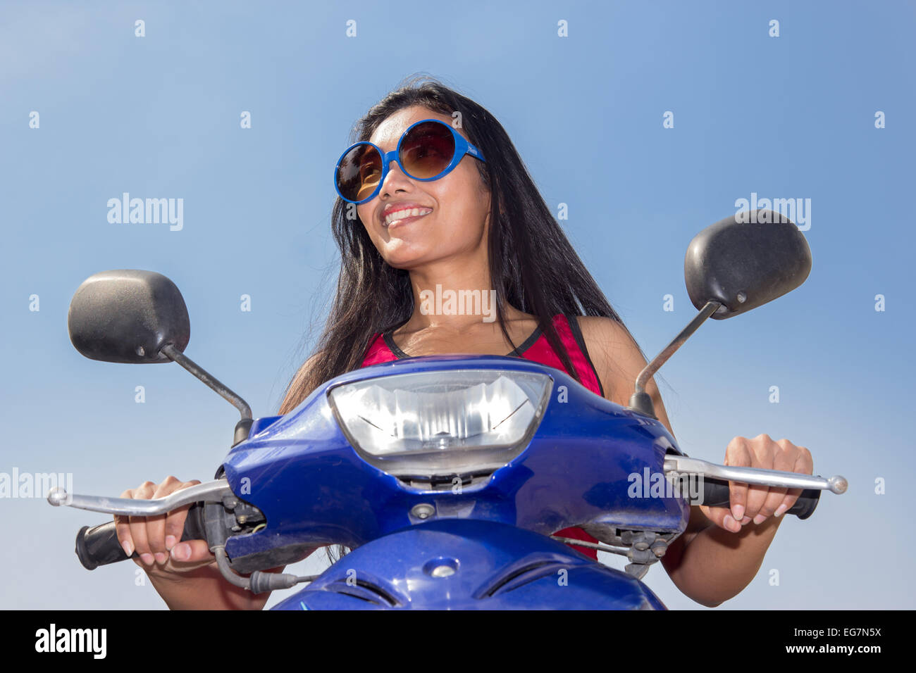 Vorderansicht einer Frau sitzt auf einem Roller auf blauem Hintergrund Stockfoto