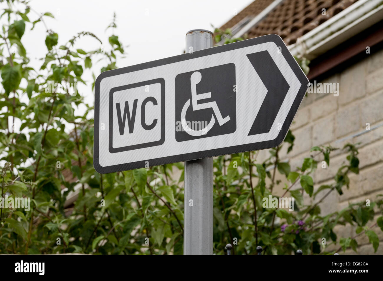Straßenschild mit Hinweis auf eine behindertengerechte öffentliche Toilette. Melden Sie sich in einem englischen Dorfparkplatz an Stockfoto