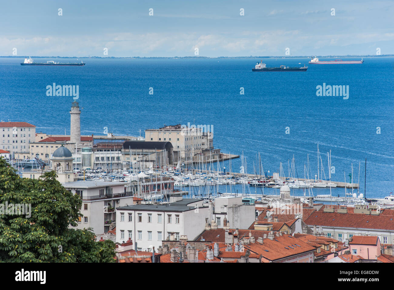 Triest, Italien - ein Blick auf den Hafen mit dem Leuchtturm von San Giusto Kathedrale gesehen. Schiffe in den Straßen vor der Küste. Stockfoto