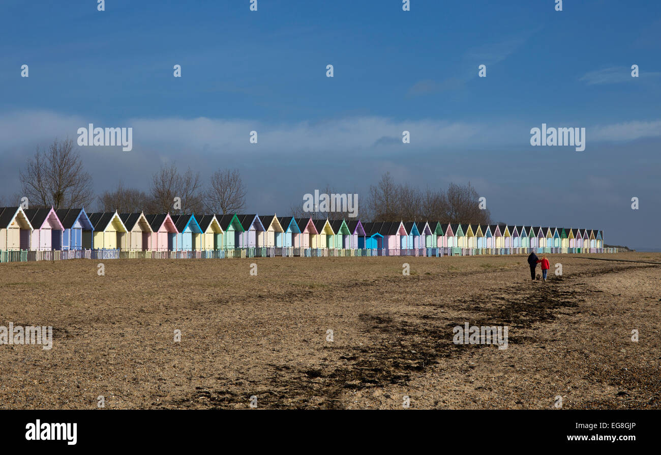 paar mit Hund Strand entlang mit bunt Strand Hütten auf Mersea Island, Essex, England Stockfoto