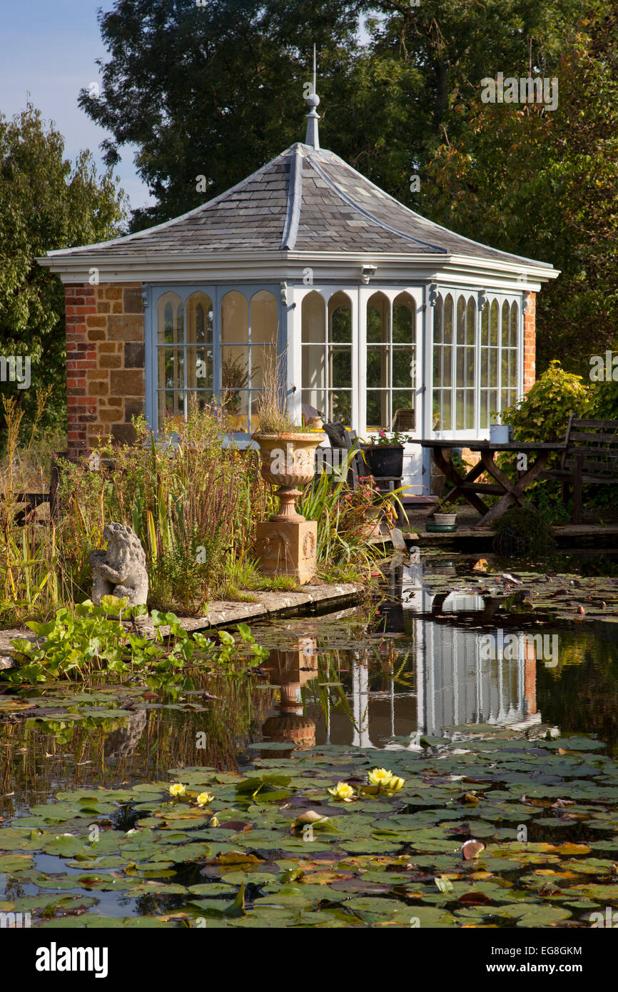Großer Gartenteich im Sommer mit gemauerten Gartenhaus und Sitzgelegenheiten mit Blick auf Wasser und Lillypads, Garten, Oxfordshire, England Stockfoto
