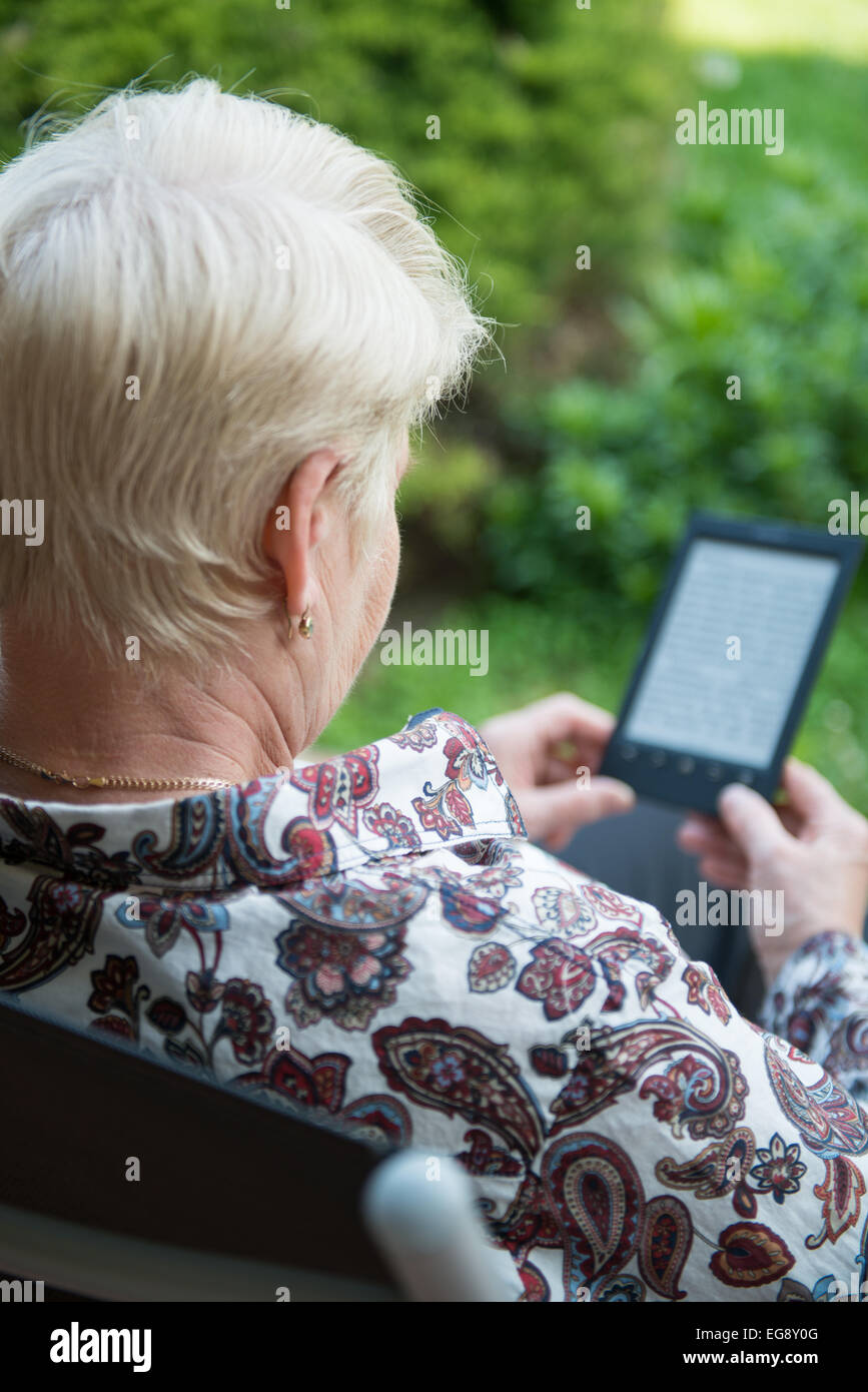 senior Seniorin im Sessel sitzen und lesen e-Book im Garten Stockfoto