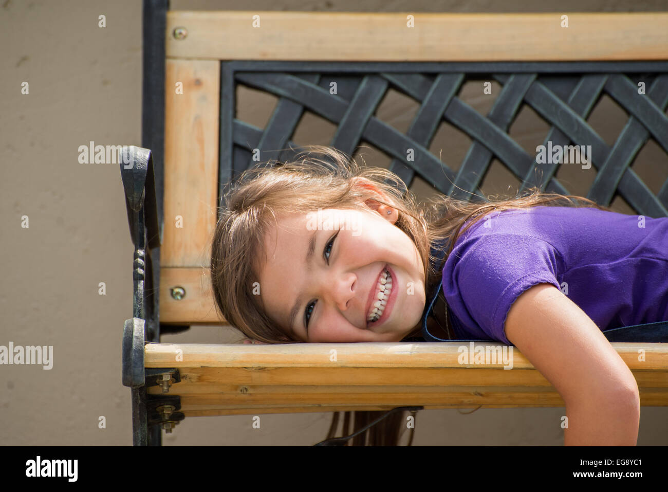 Kleines Mädchen liegend auf dem Bauch auf eine externe Bank mit einem großen Lächeln auf ihrem Gesicht. Stockfoto