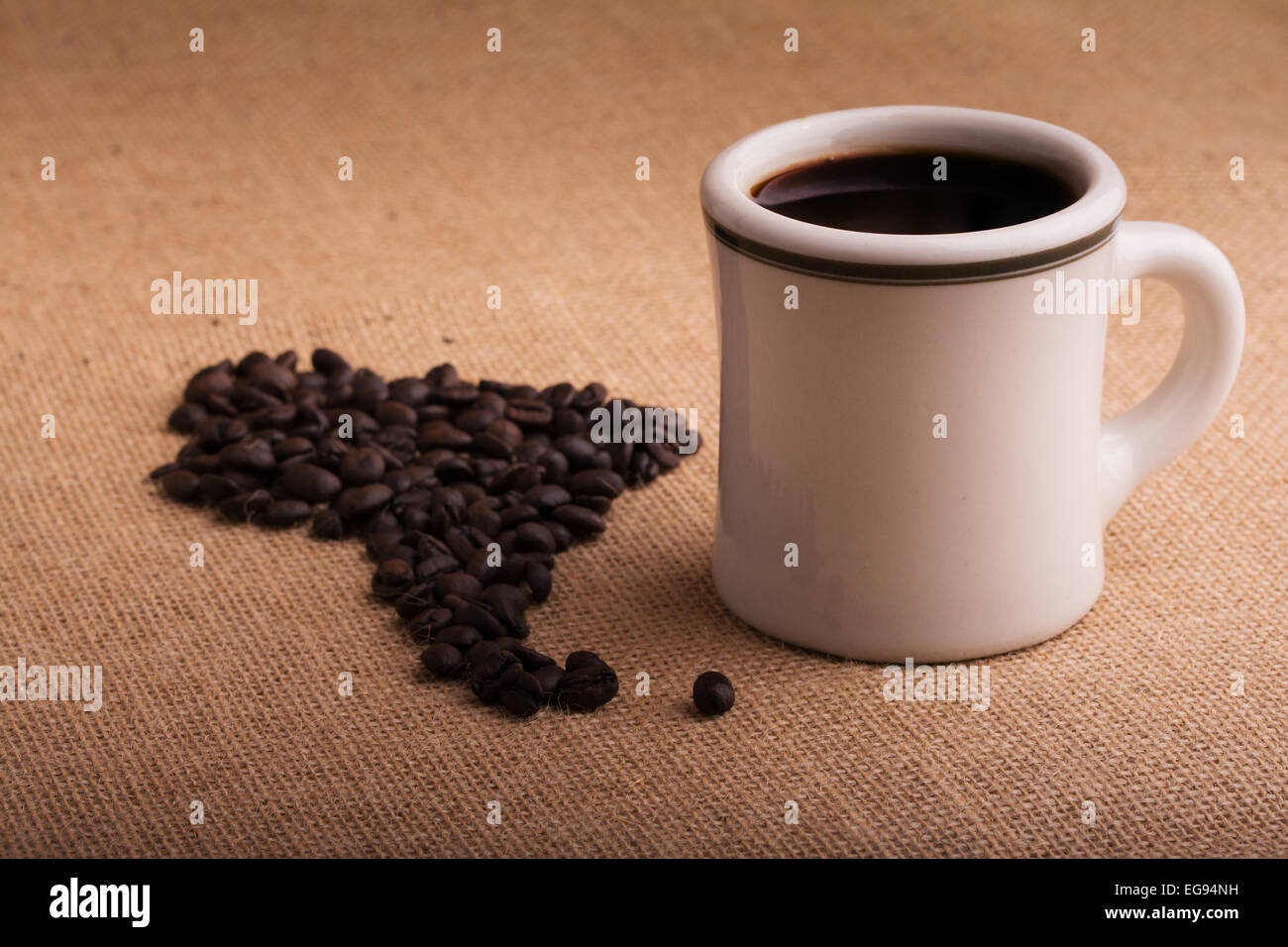 Kaffeetasse mit Bohnen in Form von Südamerika auf Sackleinen, mit einer leichten vignette Stockfoto