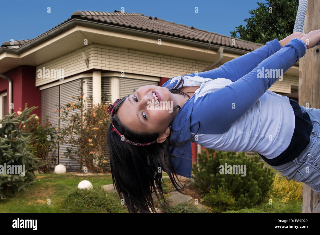 Fröhliches junges Mädchen spielen auf dem Spielplatz im Garten vor ihrem Haus. Stockfoto