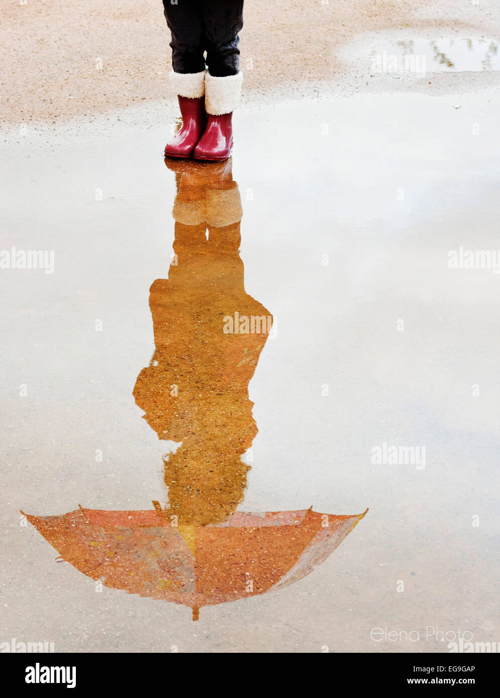 Reflexion eines Mädchens mit einem Regenschirm in einer Pfütze Stockfoto