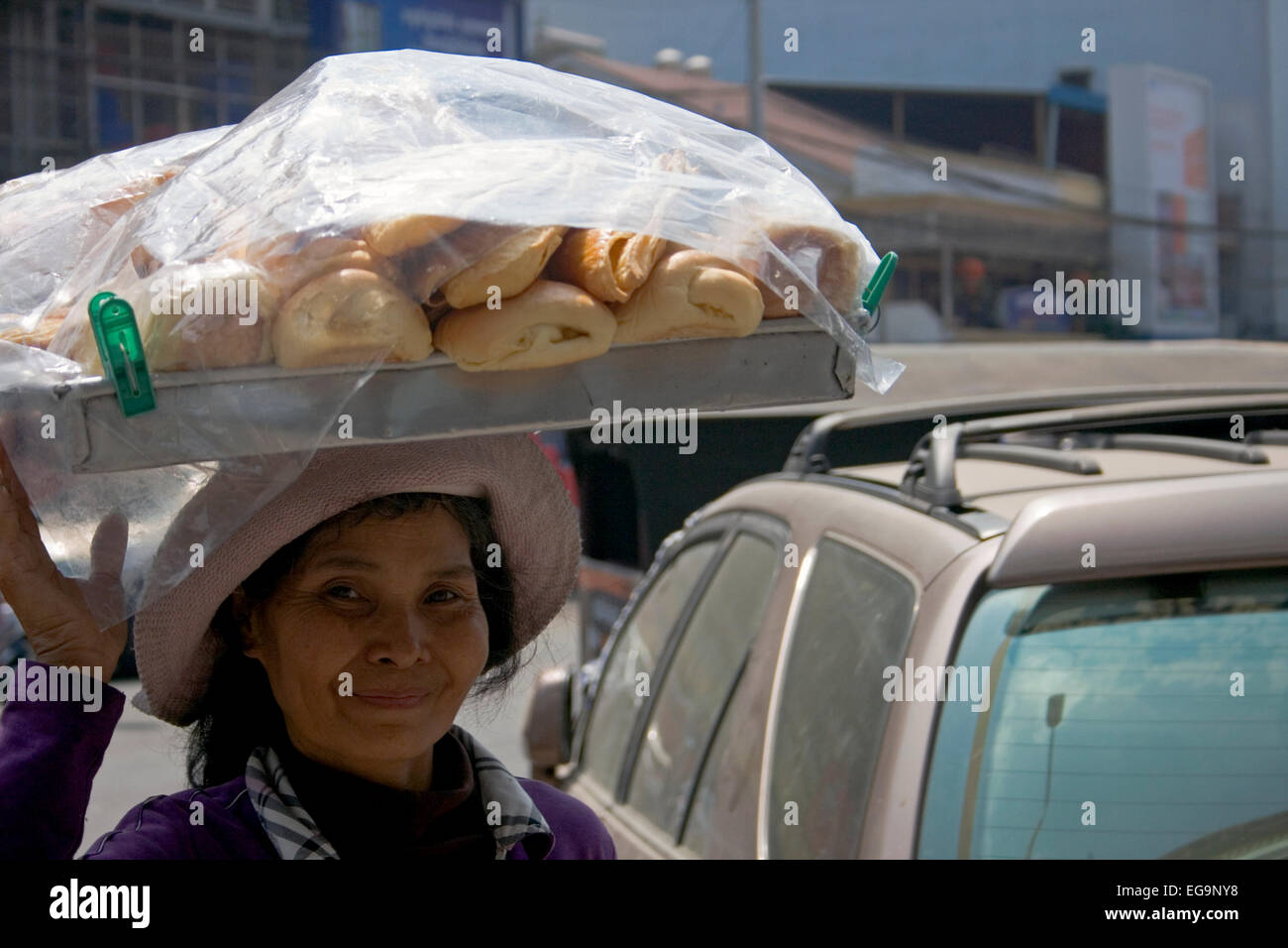 Eine Frau trägt Brot in einer Schale auf dem Kopf, die sie als Straße Nahrung auf einer belebten Straße in Phnom Penh, Kambodscha verkauft. Stockfoto