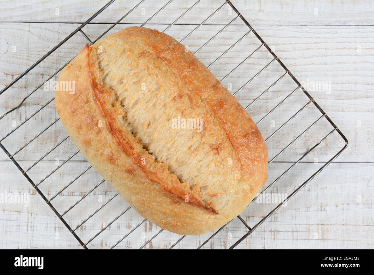 Hohen Winkel Nahaufnahme einen frisch gebackenen Laib Brot auf ein Kuchengitter. Querformat auf einem rustikalen weiß getünchten Küchentisch, wi Stockfoto