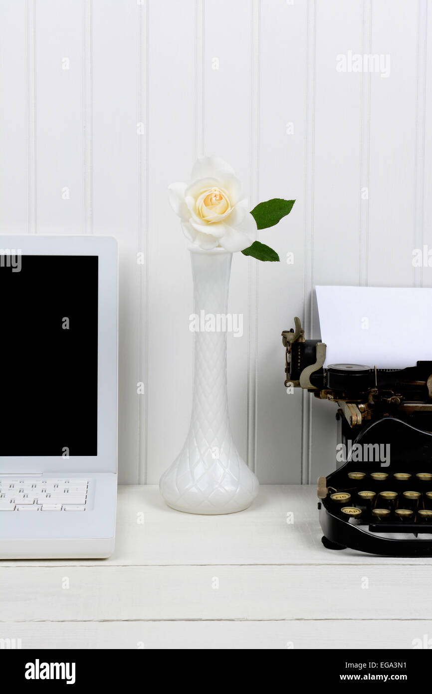 Nahaufnahme von einem weißen Schreibtisch mit einer Knospe Vase zwischen einem modernen Laptop-Computer und eine antike Schreibmaschine. Nur die Hälfte des Laptops und Stockfoto